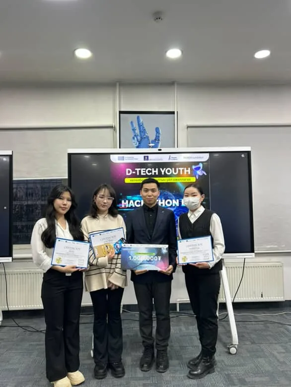 Four participants with certificates in front of the D-Tech Youth hackathon screen